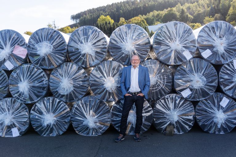The managing director of the company stands in front of large rolls wrapped in transparent plastic film.